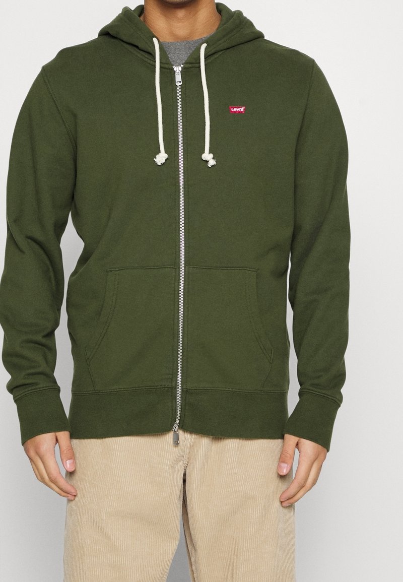 Felpa verde con zip e cappuccio regolabile, tasche a marsupio e piccolo logo rosso Levi's sul petto. Polsini e orlo standard.