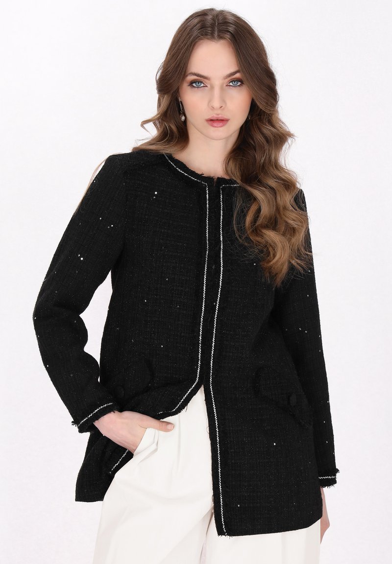 Jachetă din tweed negru cu țesătură texturată, cusături albe contrastante, două buzunare frontale și un design fără guler. Mâneci lungi, croi ajustat.