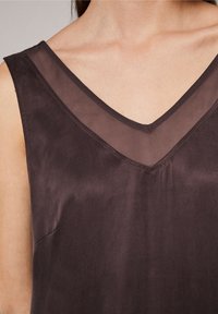 Haut sans manches violet foncé avec un décolleté en V, comportant un panneau en maille transparente au niveau du col et une texture lisse semblable à du satin.