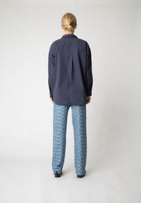 Navyblauses Langarmshirt mit subtiler Textur und Zwei-Knopf-Manschetten, kombiniert mit gemusterten blauen Hosen mit geometrischem Design.