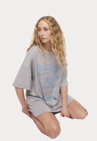Szara, oversize koszulka z krótkim rękawem, zdobiona niebieskim nadrukiem przedstawiającym Snoopiego z butelką. Wykonana z miękkiego materiału i o luźnym kroju.