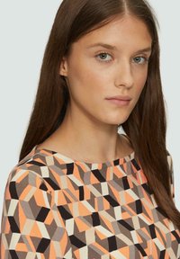Multikleurige geometrische patroon top met tinten oranje, bruin en beige, met een ronde halslijn en een soepele stofstructuur.