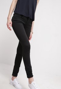 Jeans negros ajustados de cintura alta, con dobladillos enrollados, combinados con una blusa azul marino holgada y zapatillas blancas. Textura de tela suave.