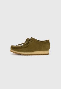 Zapato de ante verde oliva con punta redonda, diseño de cordones y suela de goma baja y texturizada. Detalle de costura mínima a lo largo del borde.