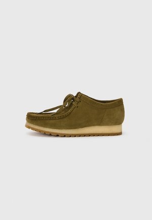 Pantofii din suede verde măsliniu, cu vârf rotund, design cu șireturi și talpă joasă din cauciuc texturat. Detaliu de cusătură minim pe margine.