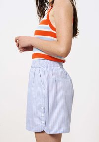 Gestreepte gebreide tanktop in oranje, blauw en wit; gecombineerd met lichtblauwe en witte gestreepte shorts met een elastische taille en knoopdetail.
