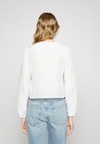 Haut court blanc à manches longues bouffantes, avec une texture légère et un col rond. Associé à un jean taille haute bleu clair.