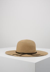Breiter Strohhut in hellem Tan mit einem strukturierten Muster, akzentuiert durch ein schwarzes geflochtenes Bändchen und zwei hängenden Riemen.