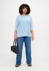 Light blue oversized shirt with three-quarter sleeves, paired with light blue wide-leg jeans, and a textured black handbag with bows.