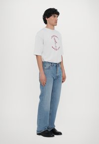 White short-sleeve t-shirt with red graphic, paired with light blue straight-leg denim jeans and black shoes. Simple design, casual fit.