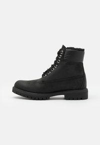 Zwarte leren enkellaarsjes met een gestructureerde afwerking, robuuste zool en metalen vetergaatjes, voorzien van een zachte fleece voering bij de kraag.
