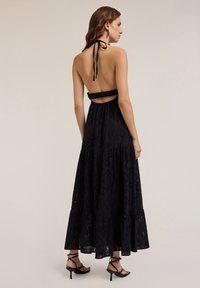 Rochie maxi neagră cu guler halter și spate deschis, cu accente volănașe și un design în straturi, realizată dintr-un material texturat.