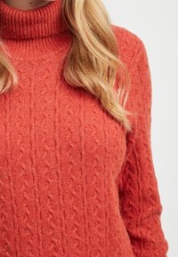 Strickpullover mit Stehkragen in Korallenfarbe, mit einem strukturierten Zopfmuster und ribbeltem Kragen. Warmes, weiches Material mit lockerer Passform.