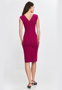 Dopasowana, do kolan sukienka w kolorze magenta z krótkimi rękawami, dekoltem w kształcie litery V na plecach i zapięciem na zamek z tyłu. Gładka tekstura, czyste linie i brak widocznych wzorów.