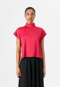 Red short-sleeve top with a high collar, made of smooth fabric, paired with a black flowing skirt, presented against a neutral background.