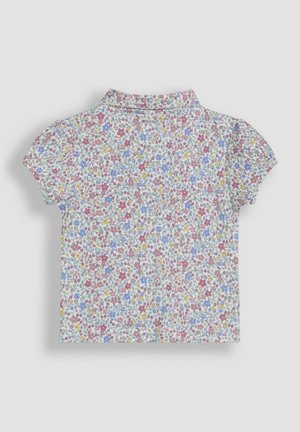 Camisa de manga corta con cuello, fabricada en un tejido blanco cubierto de pequeños patrones florales en rosa, azul y amarillo. Textura suave, diseño ligero.