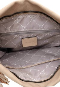 Interior de un bolso de mano de cuero beige que presenta un forro con patrón gris claro, un bolsillo con cremallera y una etiqueta de marca texturizada.