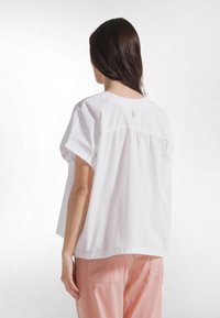 Top blanco de manga corta con cuello redondo, corte holgado y detalle fruncido en la espalda. Tela suave y ligera; diseño minimalista.