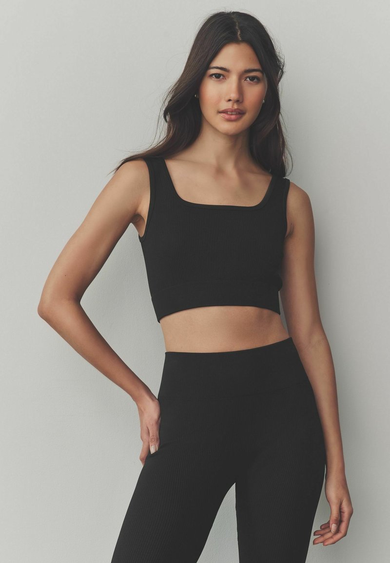 Black ribbed crop top featuring a square neckline, paired with high-waisted ribbed leggings, both made of stretchy fabric.