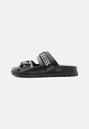 Sandalo nero a ciabatta con due cinturini regolabili, fibbie in metallo, suola spessa scanalata e logo GUESS sulla fascia superiore.