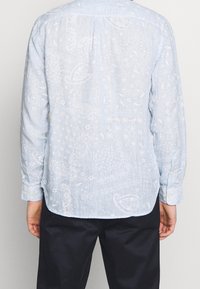 Jasnoniebieska koszula z długim rękawem, z wzorem paisley i kwiatowym, z zaokrąglonym dołem, uszyta z fakturowanej tkaniny.