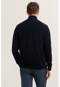 Ciemnogranatowy sweter z prążkowanym kołnierzem i mankietami, o gładkiej fakturze i dopasowanym kroju, ukazany od tyłu na jasnym tle.