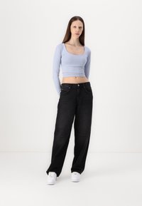 Lyseblå langermet crop topp kombinert med løstsittende svarte jeans og hvite joggesko. Personen står foran en enkel hvit bakgrunn.