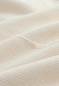 Tissu blanc à côtes avec une texture douce, présentant de légères lignes diagonales et un léger brillant, créant une apparence motif sur des couches superposées.