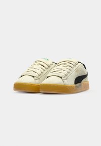 White canvas sneakers with a black side stripe, textured gum rubber sole, and rounded toe; features thick laces and minimal branding.