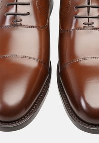 Bruine leren dresschoenen met een gepolijste afwerking, met een cap-toe ontwerp en donkere veters. Bevat gedetailleerde stiksels langs de zool.