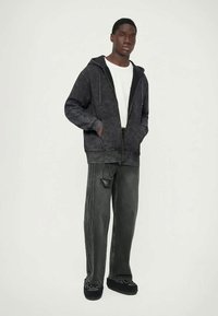 Černá mikina s kapucí a šňůrkami, texturovaná látka, v kombinaci se šedými volnými džíny s panelem a kontrastním vzorem.