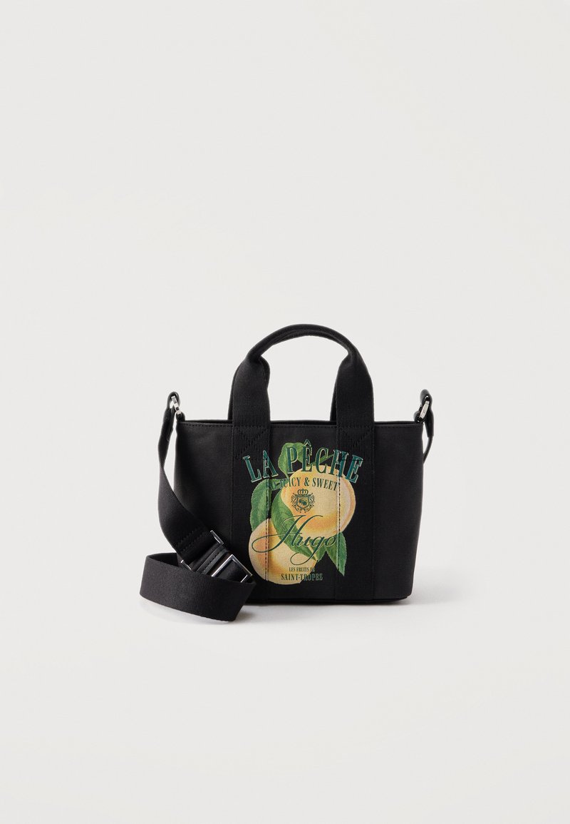 Sac à main en toile noire avec bandoulière détachable et motif imprimé de deux pêches ainsi qu’un texte en français sur le devant.