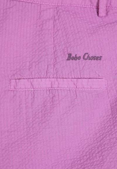 Gros plan sur un tissu lilas texturé avec une poche passepoilée horizontale et "Bobo Choses" brodé au-dessus de la poche.