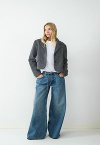 Szary, krótkowłosy wełniany żakiet z klapami, zestawiony z szerokimi dżinsami w niebieskim odcieniu, posiadającymi elastyczny pas ze sznurkiem oraz lekkim przetarciem.