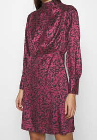 Robe à manches longues rose et noire, dotée d'un col montant, d'une taille froncée et d'un motif animal abstrait audacieux. Confectionnée dans un tissu soyeux.