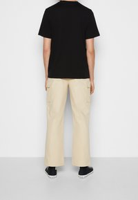 Svart t-shirt med kort ärm i kombination med beige cargobyxor. Byxorna har sidfickor och en lös passform, tillsammans med svarta sneakers.