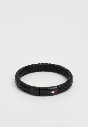 Zwarte gevlochten leren armband met een gladde sluiting en een klein gekleurd logo. Het ontwerp is rond en heeft een textuur over het geheel.