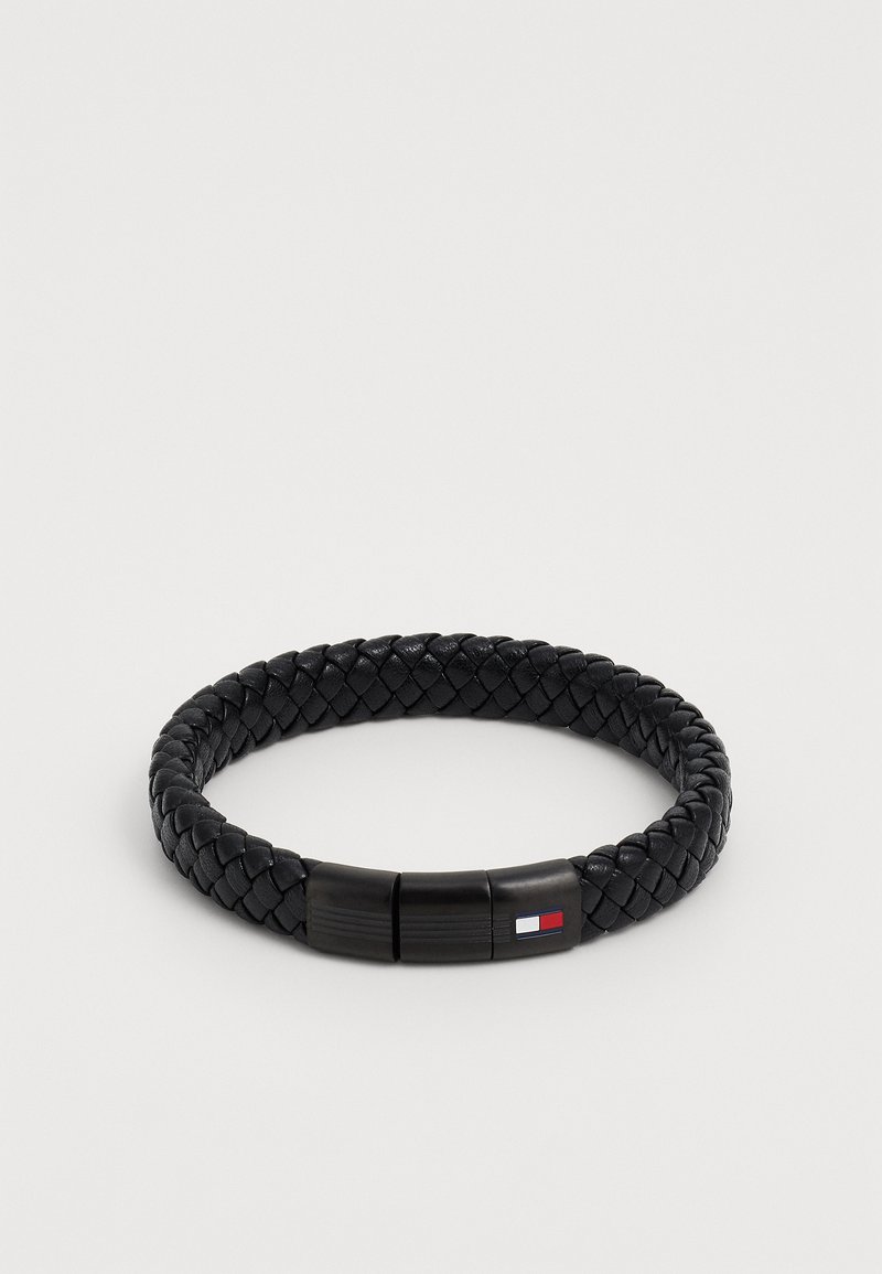 Fekete fonott bőr karkötő sima kapoccsal, amelyen egy kis színes logó található. A design kerek és texturált az egész felületen.