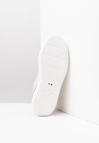 Sole di sneaker bianca con gomma testurizzata, caratterizzata da un accento dorato e un logo. Linee pulite e design minimalista con base piatta.