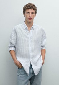 Chemise rayée gris clair à manches longues, col boutonné et poignets retroussés, associée à un jean en denim clair. Texture lisse.