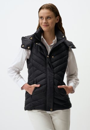 Zwarte puffer vest met een hoge kraag, een ritssluiting aan de voorkant en borstzakken. Kenmerkt zich door een gequilt ontwerp en gouden hardware accenten. Gepaard met een wit shirt.
