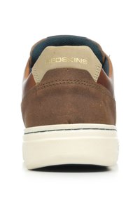 Sneaker in pelle marrone con suola bianca, caratterizzata da un accento in tessuto beige e blu scuro a contrasto sul colletto e logo in rilievo sul retro.