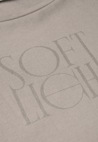 Tela de color gris claro con un estampado texturizado que dice "SOFT LIGHT" en un estilo ligeramente brillante y en relieve. Superficie suave y lisa.