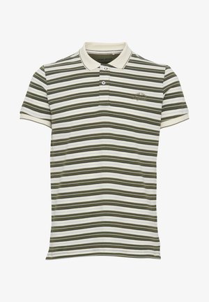 Jonge man staat met handen in zakken, draagt een groen-wit gestreept polo, bruine korte broek, witte sokken en zwarte sneakers.