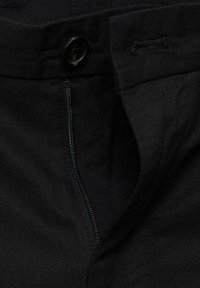 Pantalons en denim noirs avec fermeture éclair et bouton. Le tissu a une texture lisse avec des détails de couture subtils.