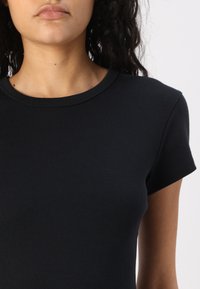 Zwarte T-shirt met korte mouwen van ribkatoen, met een ronde halslijn en een getailleerde vorm, met een gladde textuur en minimale details.
