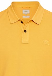 Gele poloshirt met een klassieke kraag, twee zwarte knopen en een klein geborduurd logo op de linkerborst. Gemaakt van organische materialen.