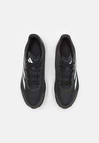 Scarpe da ginnastica nere con tomaia in rete testurizzata, lacci neri e tre strisce bianche sui lati. Suola ammortizzata per un sostegno extra.