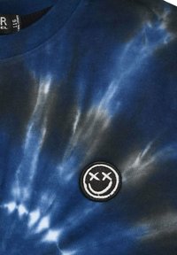 T-Shirt mit Batikdesign in Marineblau und Weiß, ausgestattet mit einem runden gestickten Patch mit einem lächelnden Gesicht. Baumwollstoff mit weicher Textur.