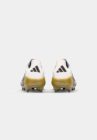 Football cleats with a white upper, purple accents, and yellow translucent sole. Features black three-stripe branding and textured patterns.